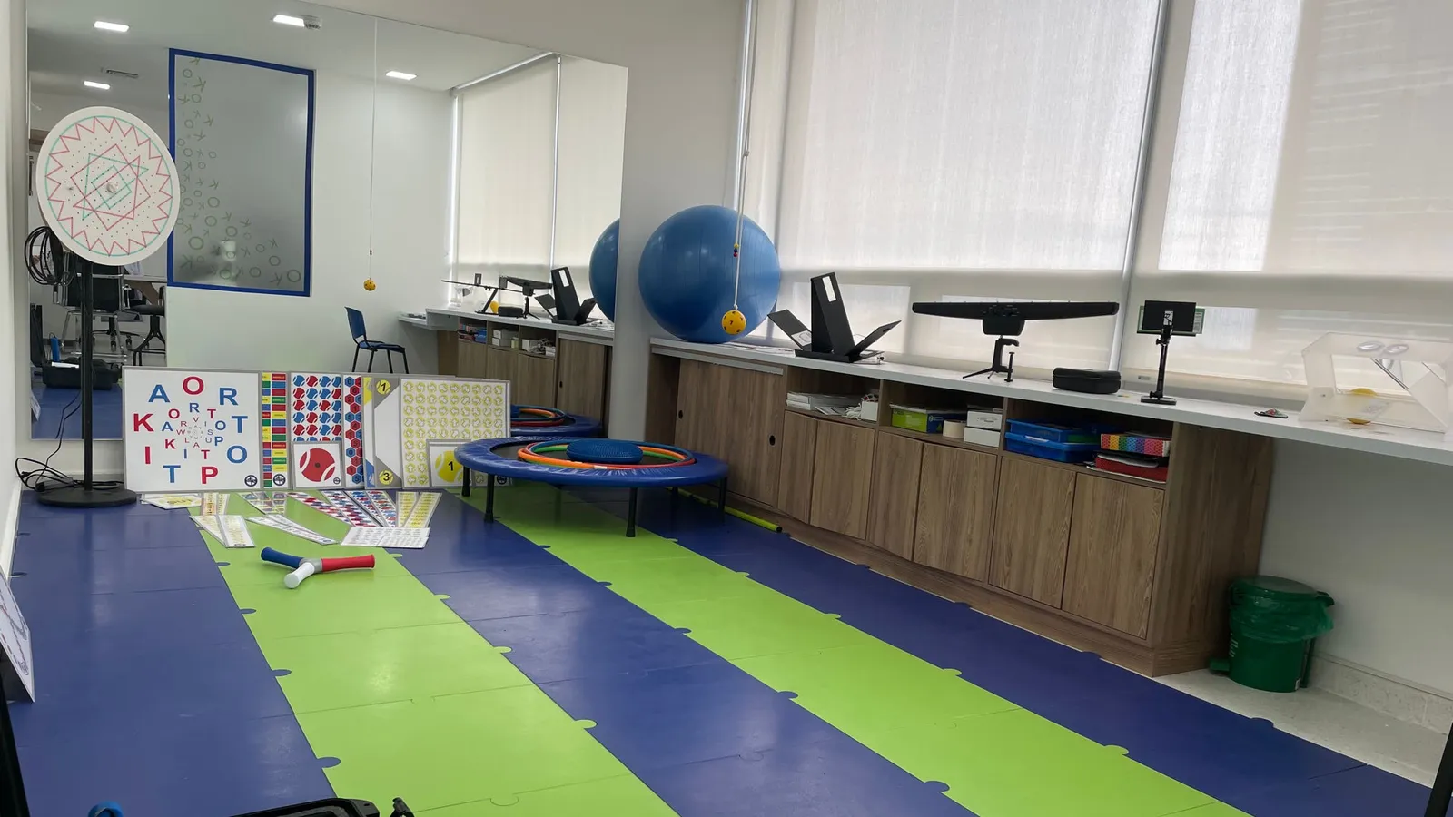 Gimnasio visual del consultorio: tapete de equilibrio, minitrampolín, balón de pilates y tabla de letras para terapia visual