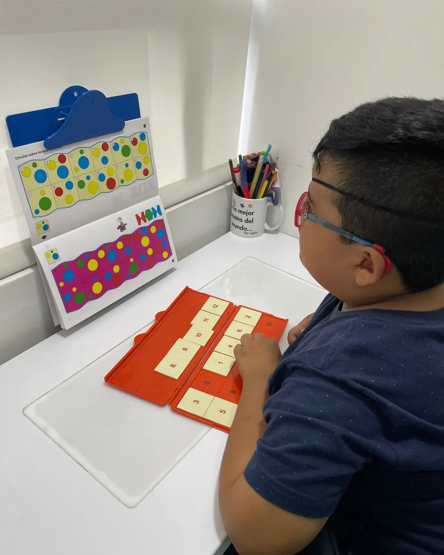 Niño con gafas resolviendo una tabla de secuencias numéricas junto a una lámina de círculos de colores