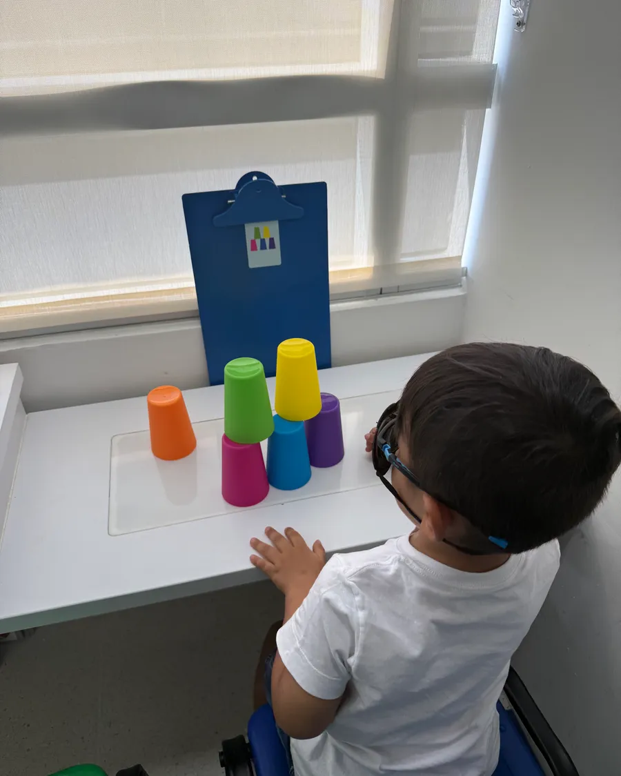 Niño con gafas ordenando vasos de colores según un patrón, ejercicio de percepción y motricidad visual